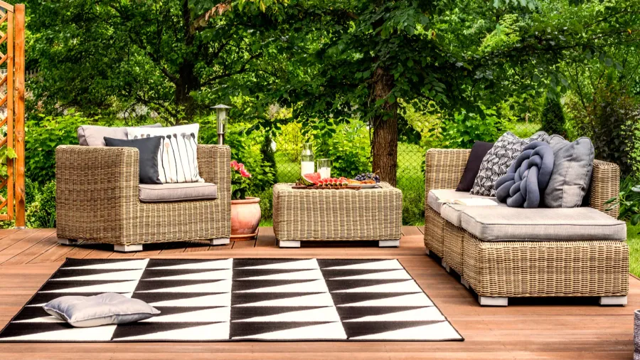 A stylish patio with rattan furniture set, different throw pillows, snacks, and a geometric rug on the wooden floor.