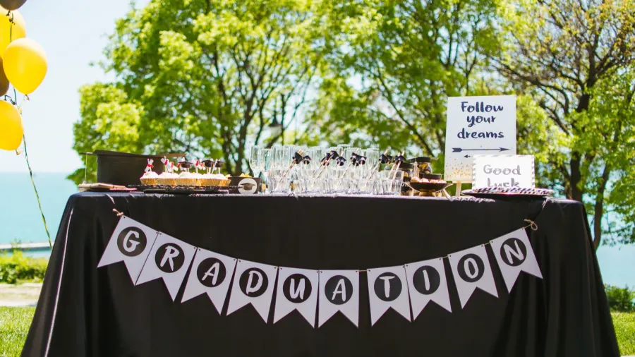 A graduation table setting with glassware, cupcakes with cute toppers, bunting, message board, and balloons.