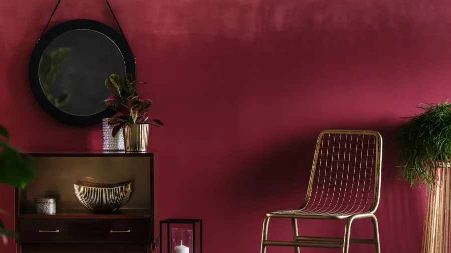 Gold chair next to a cabinet with plant against red wall with mirror in living room interior.