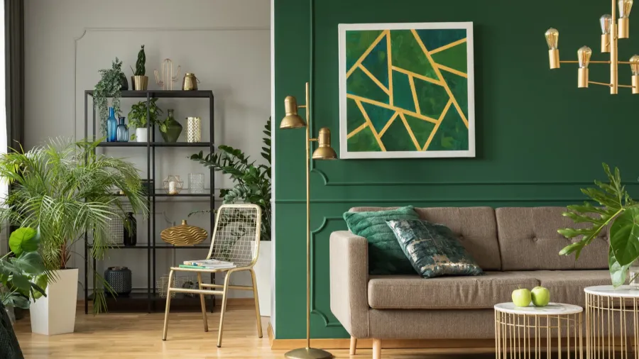 A living room interior with golden ceiling pendant light, golden floor lmp, sofa with cushions, and geometric artwork on green wall.