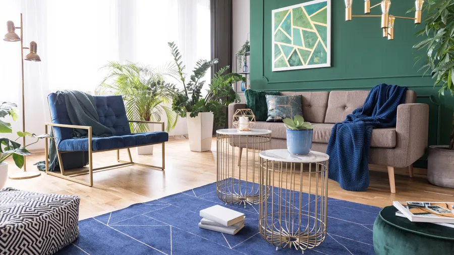 A stylish living room interior with sofa, armchair, coffee table with gold frame and marble top, lighting fixture, and plants.