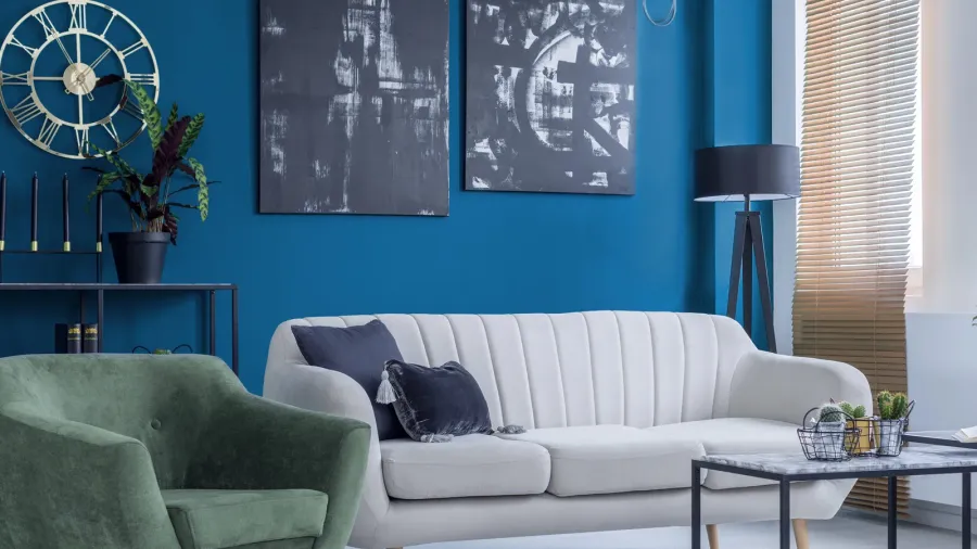 A living room interior with sofa, green armchair, coffee table, and abstract artwork on blue wall.