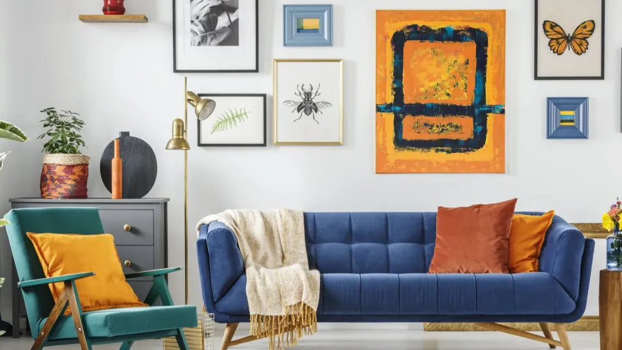A living room interior with blue sofa with throw pillows and blanket, green armchair with mustard cushion, and a gallery wall.