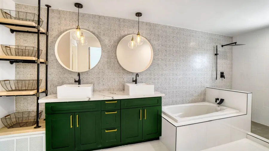 A stylish bathroom with a white marble double sink, green cabinets with yellow handles, and decorative mirrors.
