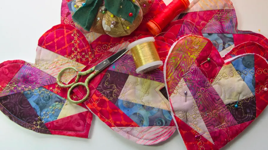 Colorful fabric pieces, scissors, pins, and sewing tools for quilting.