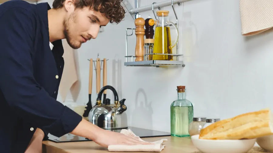 A man cleaning the kitchen counter wearing casual outfit.