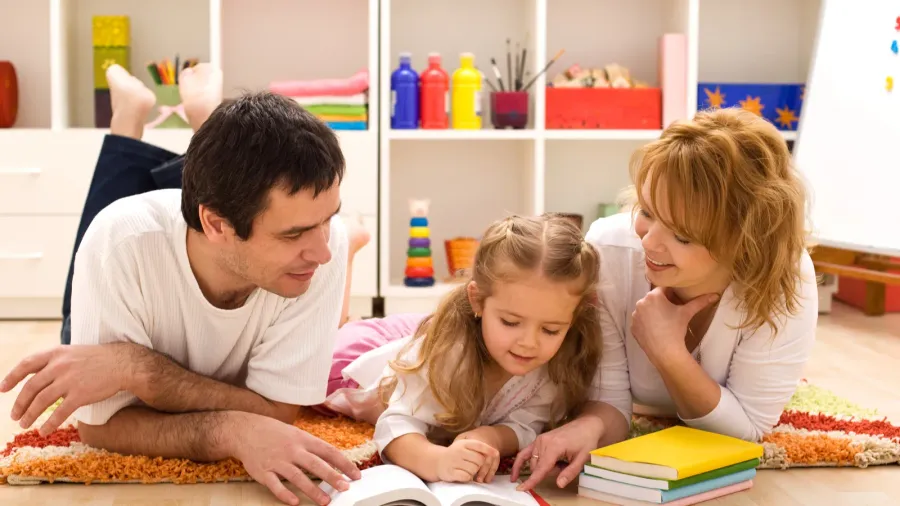 A family lying on the floor reading a book together in a cozy room.