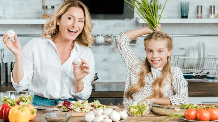 happy mother and daughter playing with food while cooking at