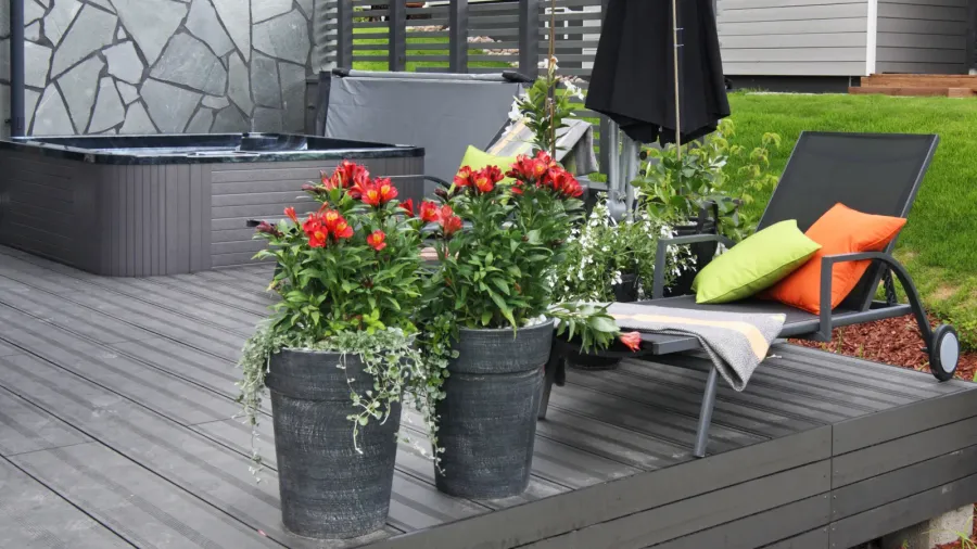 A daybed with throw pillows and blanket on a patio with flower pots near it.