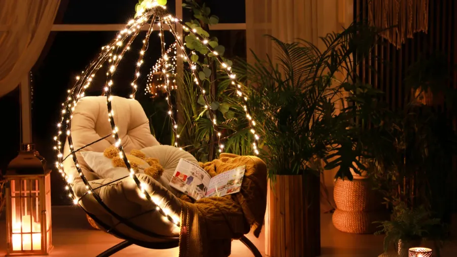 A cozy corner with a hanging chair adorned with lights and surrounded by plants.