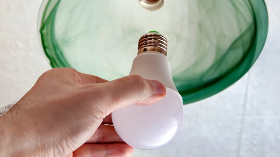 A man installing an LED bulb in a ceiling light fixture.