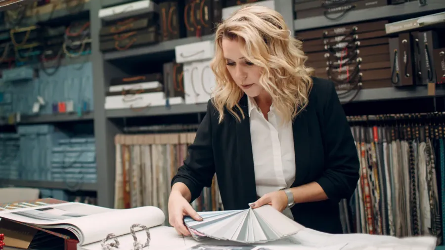 A designer holding different neutral shade color swatches with her portfolio open in front of her on a table.