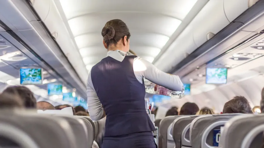interior of commercial airplane with stewardess serving passengers on seats