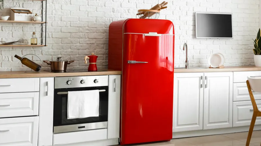 A kitchen interior with red retro fridge, white cabinets, wooden countertop, and oven.