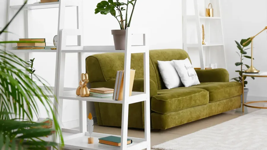 Interior of light living room with bookshelves with books, potted plant, and metallic sculptural accent, green sofa, and rug.
