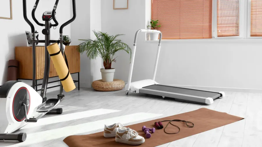 A home gym setup featuring a treadmill, yoga mat, and weights under natural light.