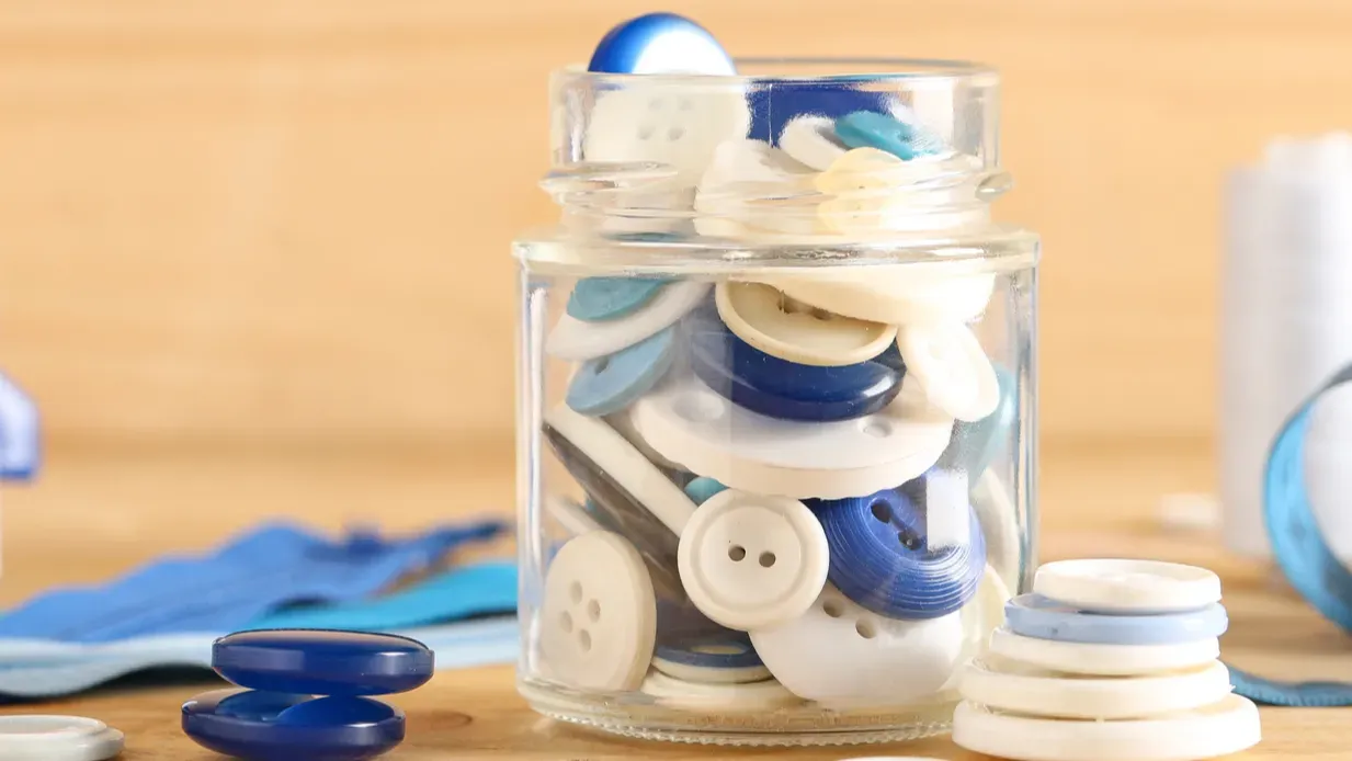 jar of different colorful buttons with supplies and manual sewing