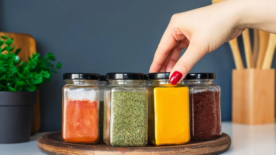 A hand reaching for a jar of spices on a kitchen counter.