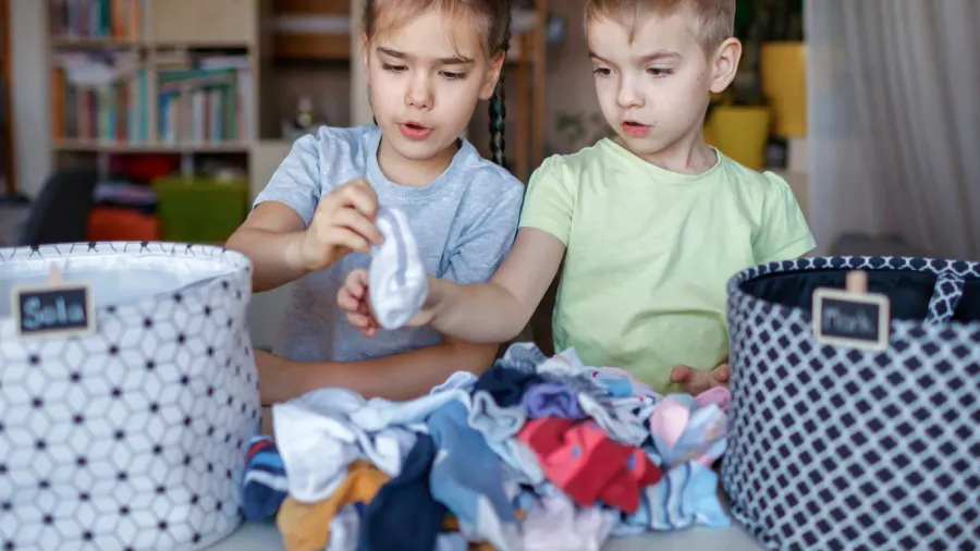 Two kids sorting their socks and putting them in labelled bins.