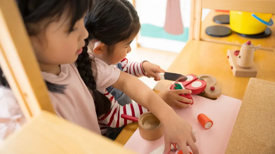 Two little girls playing in kid's play kitchen.
