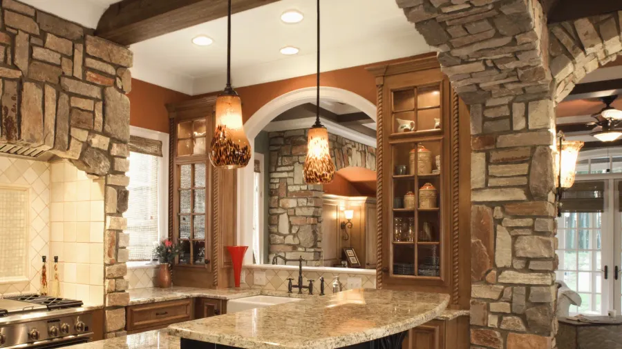 A warm, rustic kitchen with granite countertops, wooden cabinets, and stone accents on the walls.