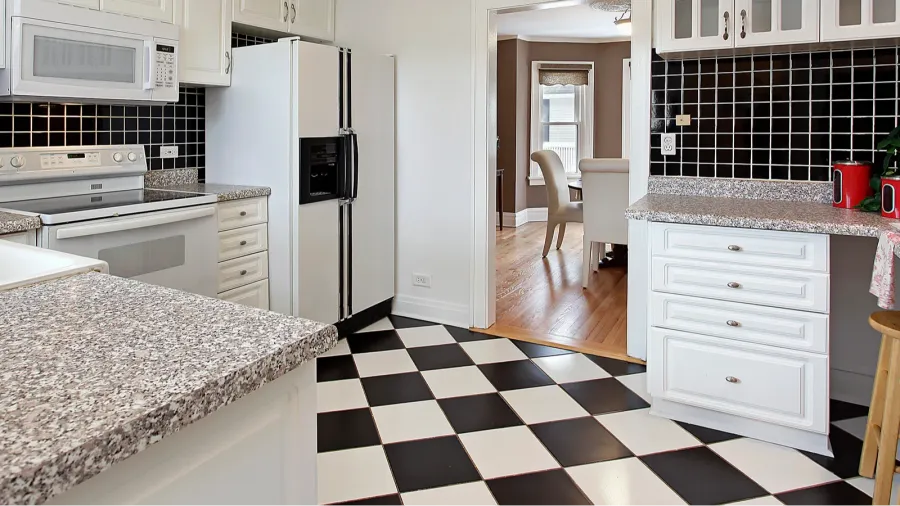 A classic kitchen presents a black and white checkered floor, white cabinets, and granite countertops for a timeless look.
