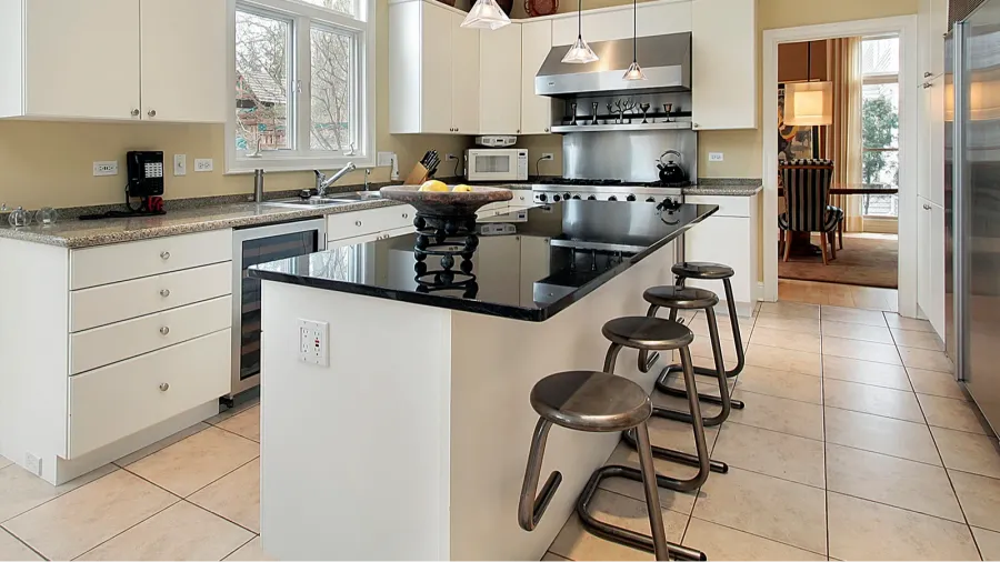 kitchen with marble island A modern kitchen with white cabinets, a black countertop island, and bar stools.