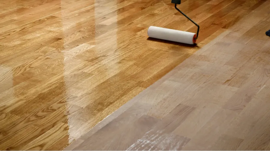 A person lacquering wood floors using a roller.