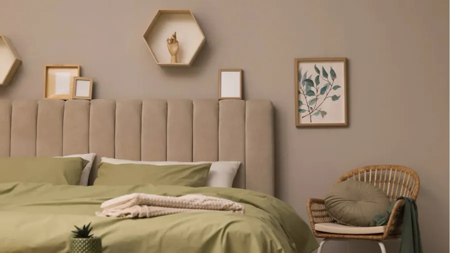 A bedroom interior with cozy bed with comforter, knitted blanket, pillows, framed artwork, and rattan armchair.