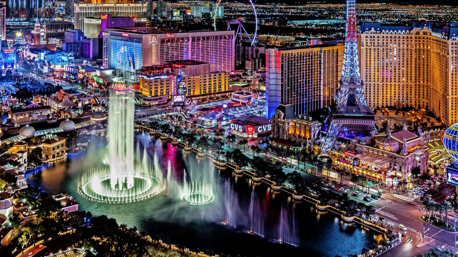 A night scene of the Las Vegas Strip, specifically highlighting the Fountains of Bellagio with the Paris Las Vegas Eiffel Tower replica in the background. 