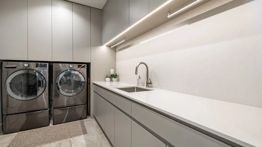 A stylish laundry room with washing machine, dryer, sink, and under-the-cabinets LED light.