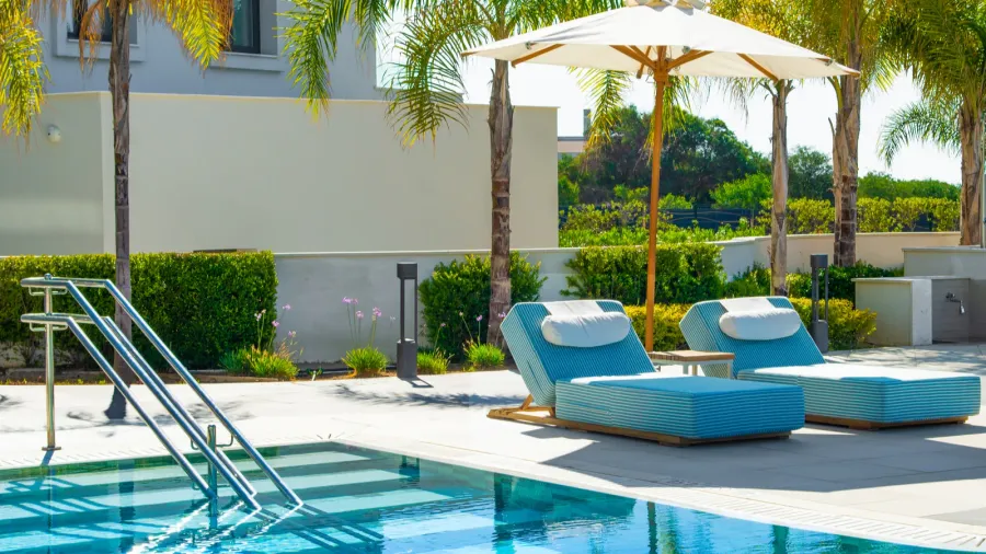 Two lounge chairs with cushions and umbrella by an outdoor pool.