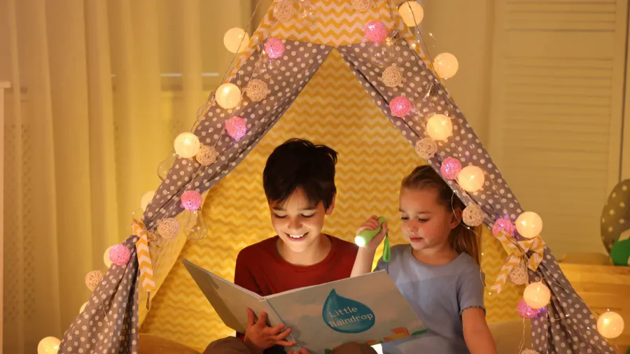 little children with flashlight reading book in play tent at