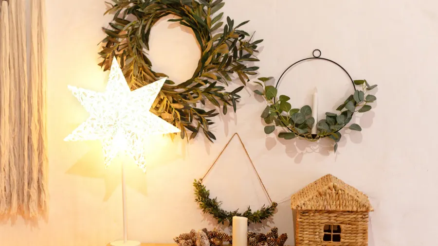 Living room with a wooden chest of drawers and wicker. Wreaths, star light, and candles and pinecones are hanging and placed on the chest.