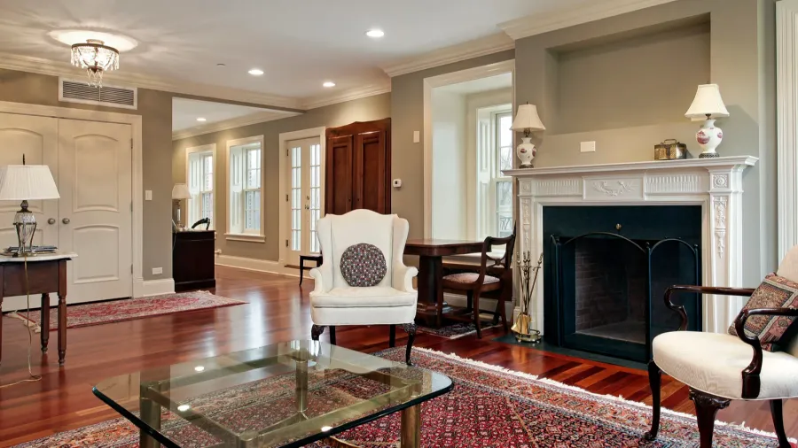 A living room interior with hardwood flooring, coffee table, armchairs, fireplace, and a Persian area rug.
