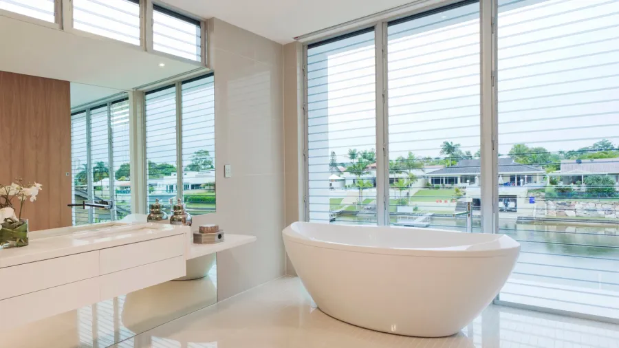 A modern bathroom featuring a white tub by large windows overlooking a serene view.