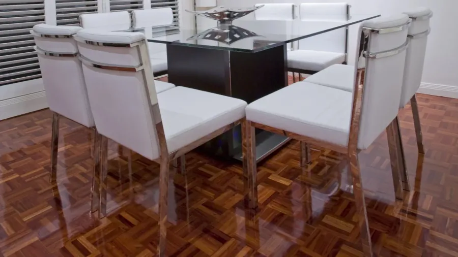 A dining room interior with polished hardwood floor, glass table, and chairs.