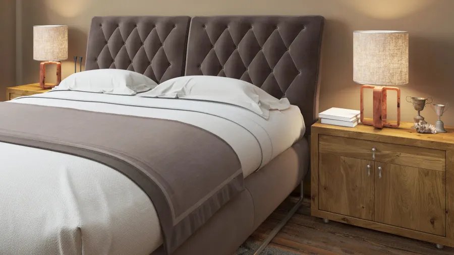 The image features a plush tufted headboard and layered bedding, creating a cozy bedroom ambiance. A wooden nightstand holds a textured lamp and decorative items, enhancing the modern aesthetic.