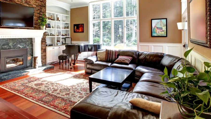 A luxury living room interior with leather sofa, dark wood coffee table, rug, piano, and fireplace.