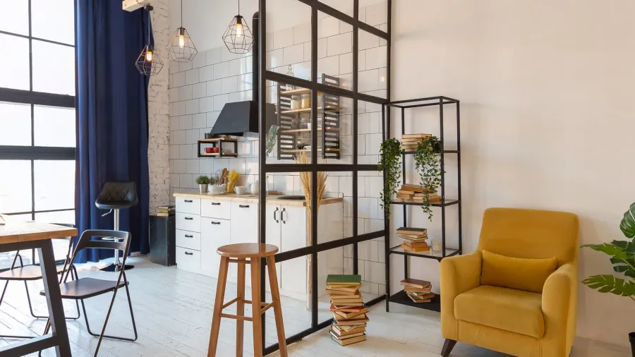 A modern kitchen and living space separated by a black glass partition.