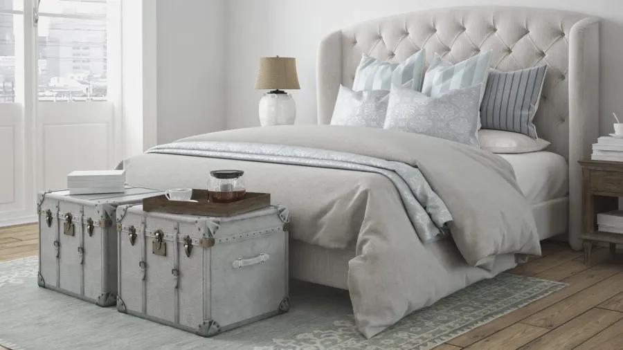 A well-decorated bedroom with a tufted headboard, plush bedding, and decorative trunks used as side tables.