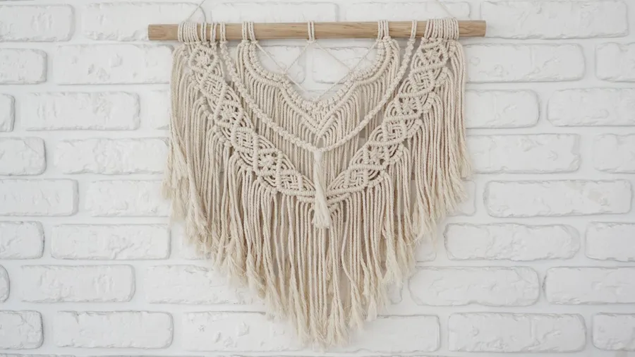 A beautiful woven macrame wall hanging on a white brick wall.