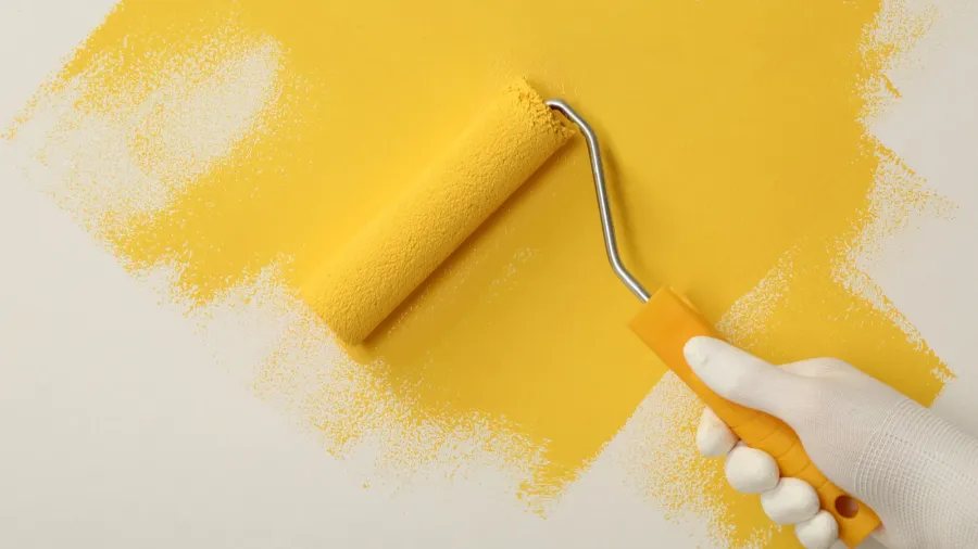 A man applying yellow paint with roller brush on a white wall.