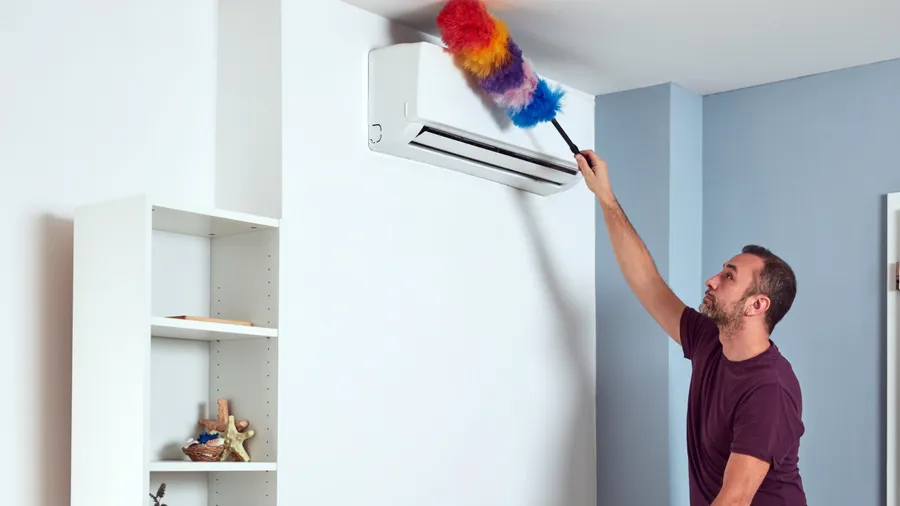 A man dusting the AC unit using a colorful duster.
