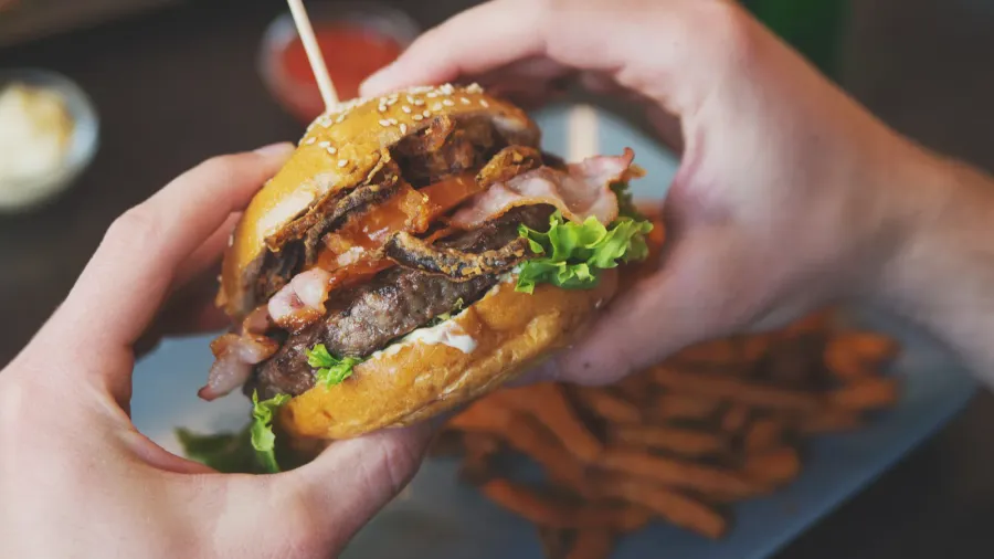 man holds burger with hands and sweet potato fries
