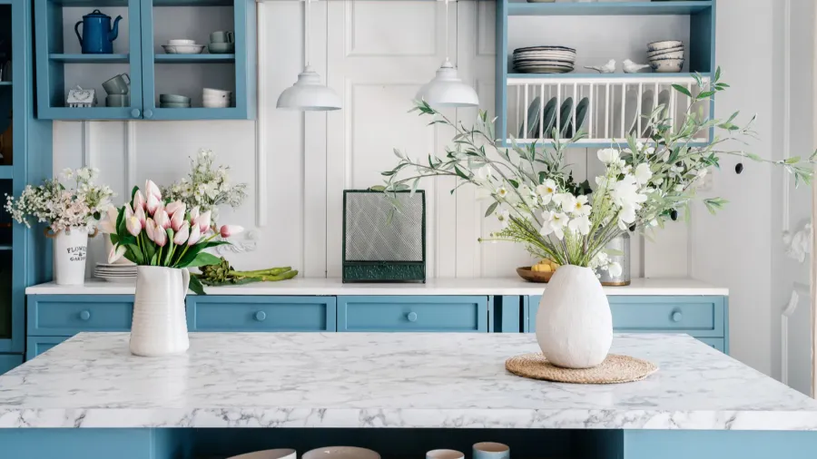 Bright kitchen with blue cabinetry, white marble countertop, and decorative flowers in vases.