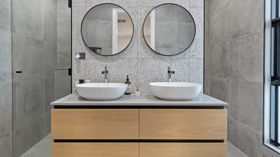 A wooden vanity with double sink in front of a marble tiled backsplash.