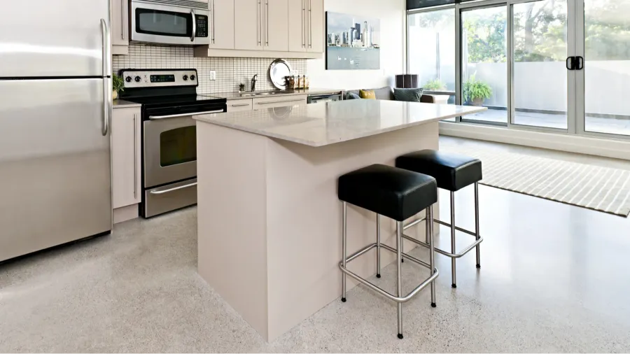 A kitchen interior with white cabinets, marble countertop, and a floating island with barstools.