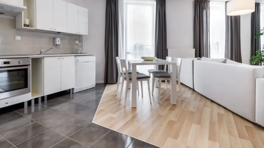 A modern kitchen and dining area showcasing white cabinetry, a sleek countertop, and a blend of tile and wood flooring.