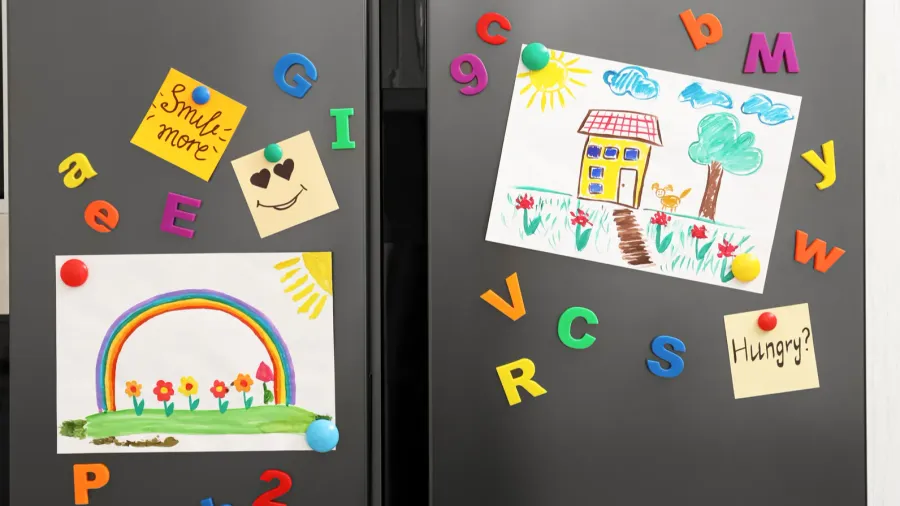 A modern refrigerator in a kitchen with child's drawings, notes, and magnets.